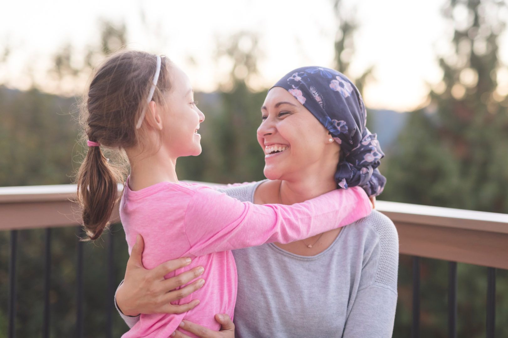 A girl in a pink shirt hugging a smiling woman who is wearing a headscarf